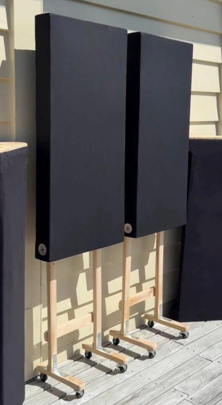 Two acoustic panels on castor stands leaning against a house exterior