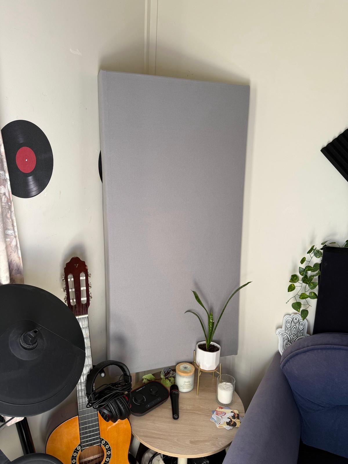 Grey acoustic panel installed in a home music studio corner, beside guitars and a turntable